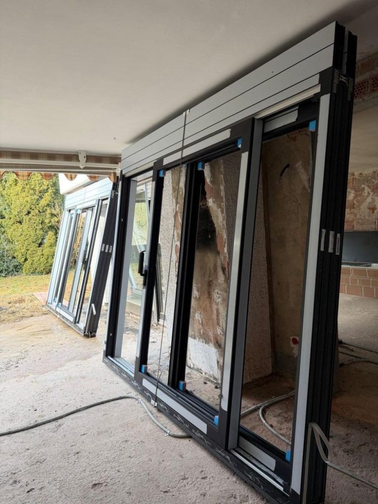 Mehrere neue Fenster stehen vor der Fenstermontage bei einer Gebäudesanierung an einer Wand.